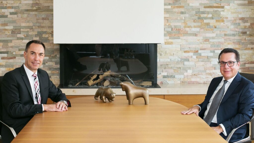 Michael Geiß (links) und Reiner Riecker von der Hoerner Bank sitzen sich an einem Holztisch gegenüber, zwischen ihnen Bronzefiguren von Bulle und Bär
